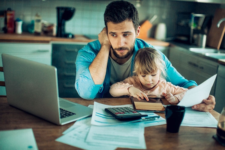 A man with his son sitting on his lap. He is looking at a laptop with a concerned look on his face. 